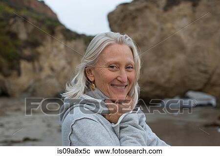 Stock Image - Mature woman wearing grey sweater on beach, smiling. Fotosearch