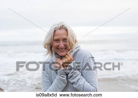 Stock Image - Mature woman wearing grey sweater on beach, smiling. Fotosearch