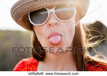 Mature woman wearing sunglasses and sunhat sticking out tongue View Large Photo Image Stock Photograph - Mature woman wearing sunglasses and sunhat sticking out tongue. Fotosearch