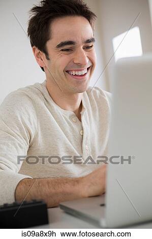 Stock Image - Mid adult man using laptop, laughing. Fotosearch