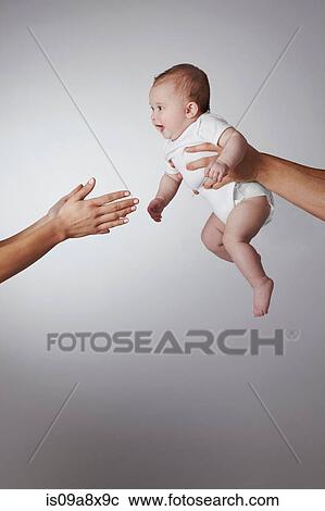 Stock Image - Parents passing baby daughter to each other. Fotosearch