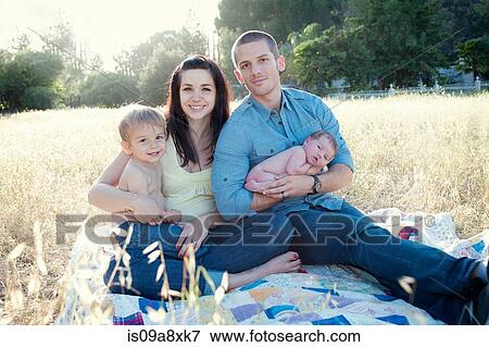 Stock Photo - Parents with son and baby daughter on blanket in field. Fotosearch