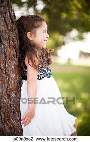 Stock Image - Portrait of girl leaning against tree trunk, smiling. Fotosearch