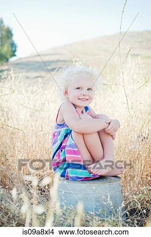 Picture - Portrait of girl sitting on bucket in field. Fotosearch