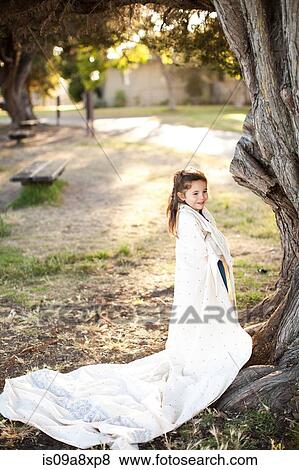 Stock Photo - Portrait of girl wrapped in sheet under tree. Fotosearch