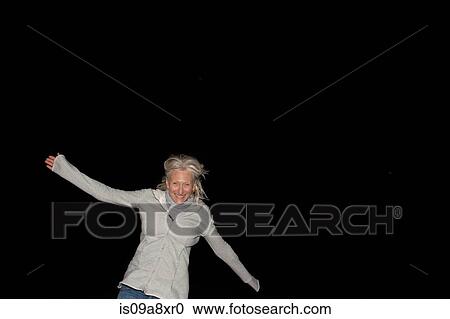 Stock Image - Portrait of mature woman with arms out at night. Fotosearch