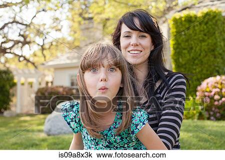 Stock Image - Portrait of mother and daughter pulling face in garden. Fotosearch