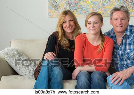 Stock Image - Portrait of mother and father with teenage daughter on sofa. Fotosearch