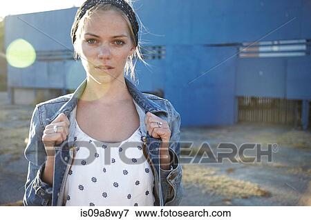 Stock Photo - Portrait of woman holding jacket collar in industrial district. Fotosearch
