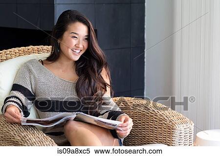 Portrait of young woman sitting on armchair with magazine View Large Photo Image Stock Photography - Portrait of young woman sitting on armchair with magazine. Fotosearch