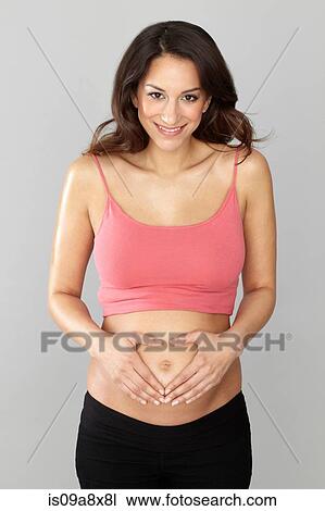 Stock Image - Pregnant woman making heart shape with hands on stomach. Fotosearch