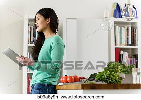 Stock Image - Profile of woman holding digital tablet leaning against table. Fotosearch