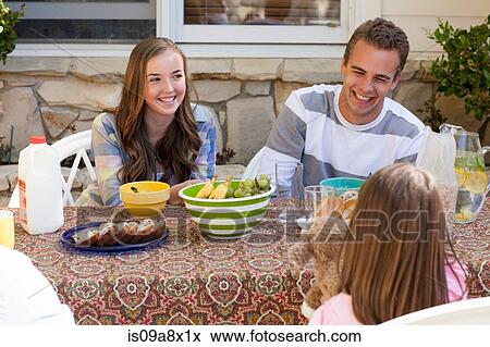 Stock Photo - Sisters and brother having breakfast outdoors. Fotosearch