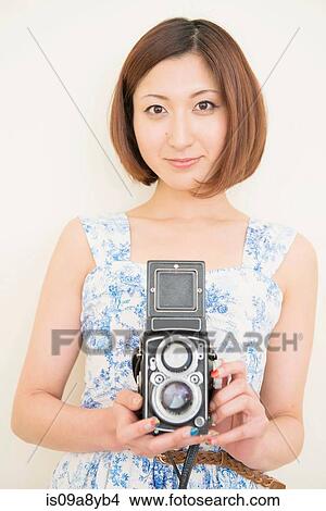 Picture - Smiling woman holding a 1960's classic camera. Fotosearch