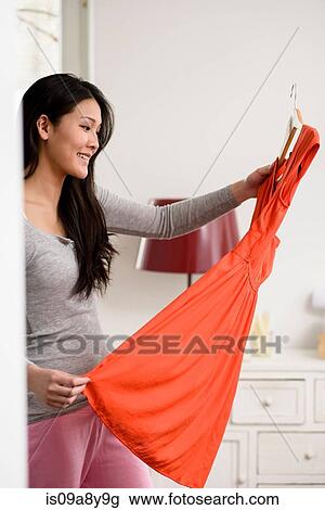 Stock Image - Smiling woman holding up orange dress. Fotosearch