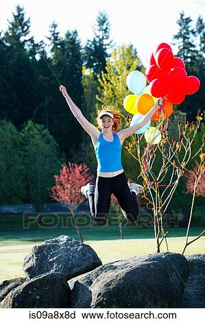 Stock Image - Teenage girl holding balloons jumping mid air. Fotosearch