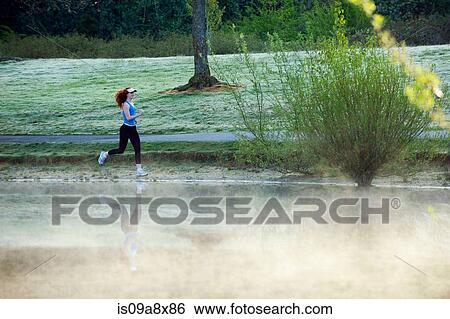 Stock Photograph - Teenage girl jogging by misty lake. Fotosearch