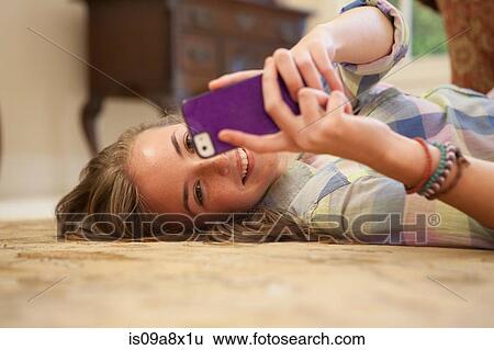 Stock Photograph - Teenage girl lying on floor with cell phone. Fotosearch