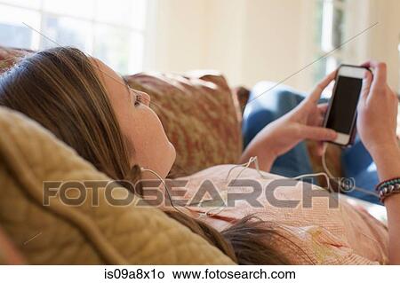 Picture - Teenage girl lying on sofa with earphones. Fotosearch