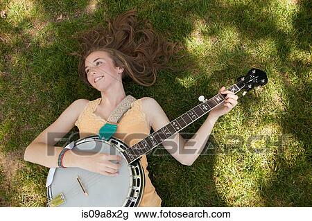 Stock Image - Teenage girl playing banjo on grass, overhead view. Fotosearch