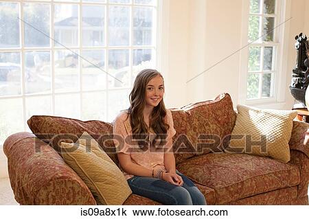 Stock Image - Teenage girl sitting on sofa, smiling. Fotosearch