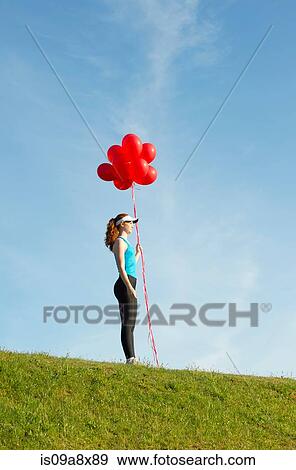 Stock Photo - Teenage girl standing on grass holding red balloons. Fotosearch