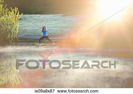 Stock Photo - Teenage girl stretching by misty lake in sunlight. Fotosearch