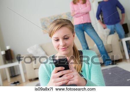 Teenage girl using cell phone, parents in background View Large Photo Image Stock Image - Teenage girl using cell phone, parents in background. Fotosearch