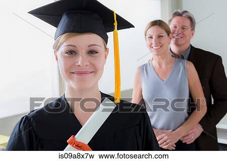 Stock Photo - Teenage girl wearing mortarboard with parents in background. Fotosearch