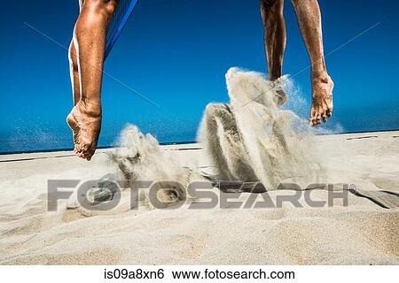 Stock Photograph - Two beach volleyball players jumping mid air in sand. Fotosearch