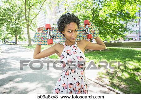 Stock Photo - Woman carrying skateboard across shoulders. Fotosearch