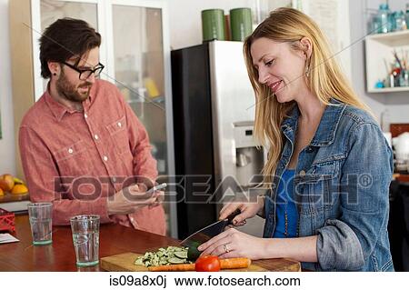 Woman chopping vegetables, man using smartphone View Large Photo Image Stock Image - Woman chopping vegetables, man using smartphone. Fotosearch