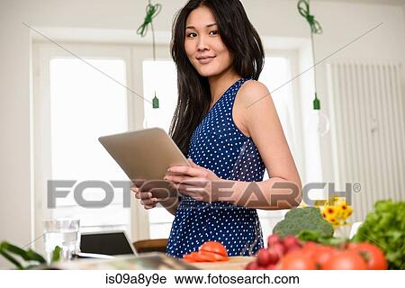 Stock Image - Woman holding digital tablet looking at camera. Fotosearch
