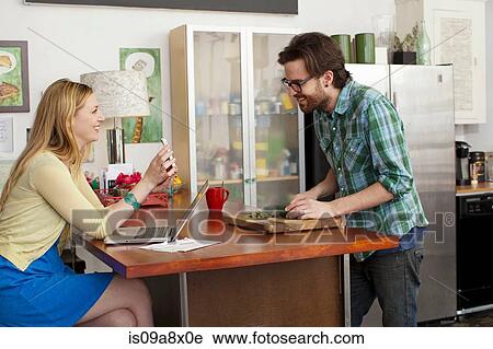 Stock Image - Woman on laptop computer, man chopping vegetables. Fotosearch