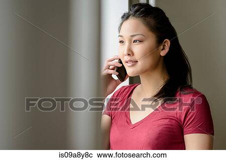 Stock Image - Woman on mobile phone looking into distance. Fotosearch