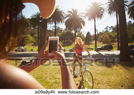 Woman photographing friend on bicycle View Large Photo Image Stock Image - Woman photographing friend on bicycle. Fotosearch
