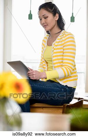 Stock Image - Woman sitting on table using digital tablet. Fotosearch