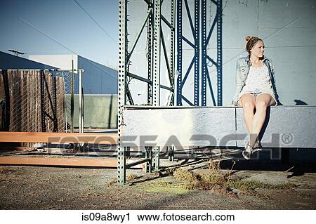 Woman sitting on wall in industrial area View Large Photo Image Stock Image - Woman sitting on wall in industrial area. Fotosearch