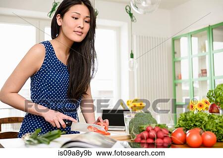 Stock Image - Woman slicing tomatoes looking at digital tablet. Fotosearch