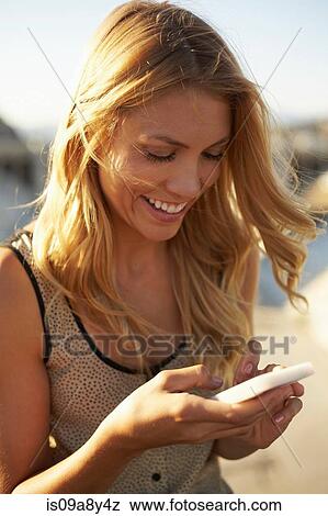 Stock Photo - Woman smiling at text message on mobile phone. Fotosearch