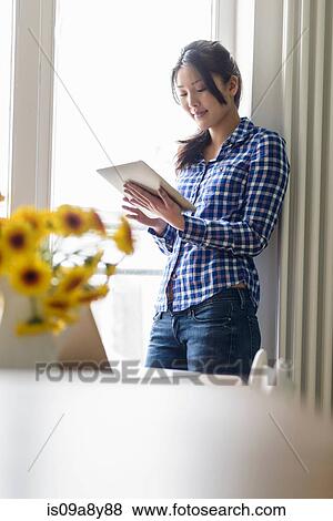Woman using digital tablet beside window View Large Photo Image Stock Photo - Woman using digital tablet beside window. Fotosearch