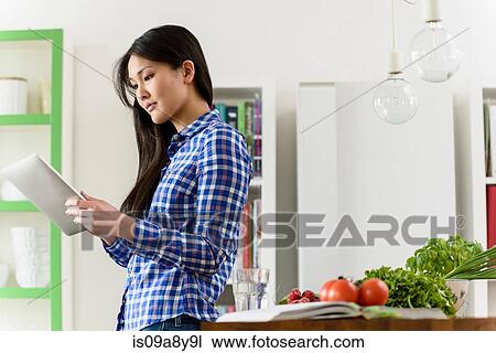 Stock Image - Woman using digital tablet in kitchen. Fotosearch