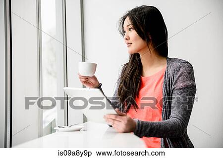 Stock Photography - Woman with digital tablet during break looking out window. Fotosearch
