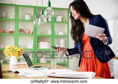 Stock Photo - Woman with digital tablet looking at mobile phone. Fotosearch