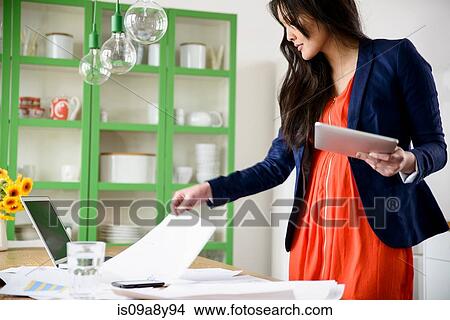 Woman with digital tablet looking through paperwork View Large Photo Image Picture - Woman with digital tablet looking through paperwork. Fotosearch