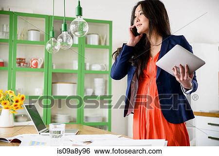 Stock Photograph - Woman with digital tablet talking on mobile phone. Fotosearch
