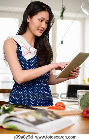Woman with tea towel over shoulder using digital tablet View Large Photo Image Stock Image - Woman with tea towel over shoulder using digital tablet. Fotosearch