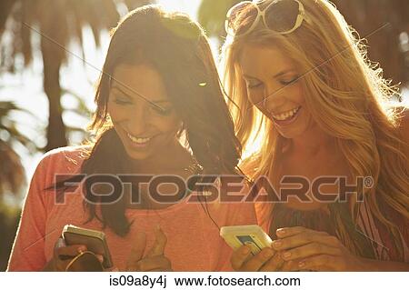Stock Image - Women sharing text messages on phone. Fotosearch