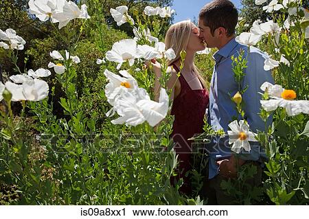 Stock Image - Young couple kissing in field with white flowers. Fotosearch
