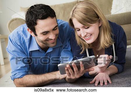 Stock Photo - Young couple lying on floor with electronic book. Fotosearch